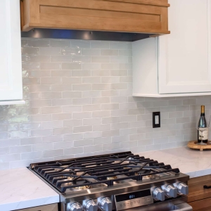 Gloss backsplash tile meeting white uppers at the range, wine glasses on the counter
