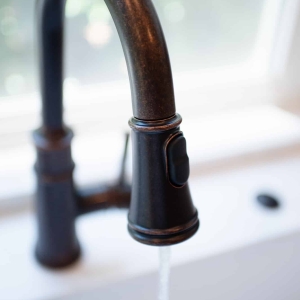 Oil-rubbed bronze pull-down faucet running water into the sink below the window
