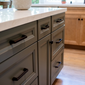 Bronze pulls across the green island fronts with maple cabinetry behind