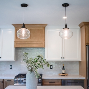Two seeded glass pendants in front of the wood hood surround and white upper cabinets