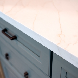 Quartz countertop edge meeting the green island drawer fronts and bronze pull