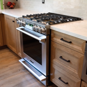 Gas range seen at an angle with maple cabinetry and drawer fronts alongside