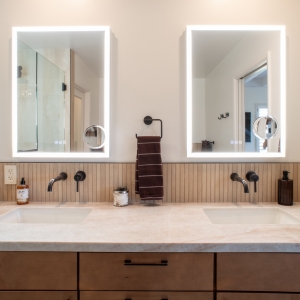 Two lighted mirrors above wall-mounted faucets and a slat tile backsplash