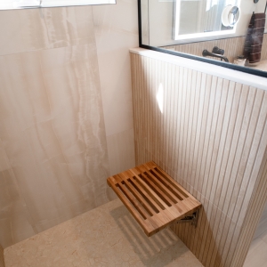 Fold-down teak shower seat above a hexagon mosaic shower floor