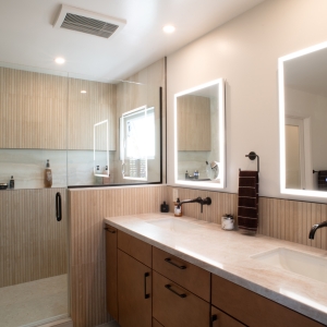 Double vanity with lighted mirrors beside a glass-enclosed walk-in shower