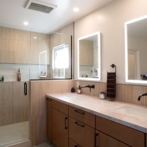 Maple vanity and glass shower panel under recessed lights and a ceiling exhaust fan
