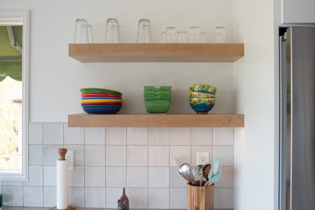 Wood floating shelves holding everyday dishes above a white tile backsplash in a Point Loma kitchen